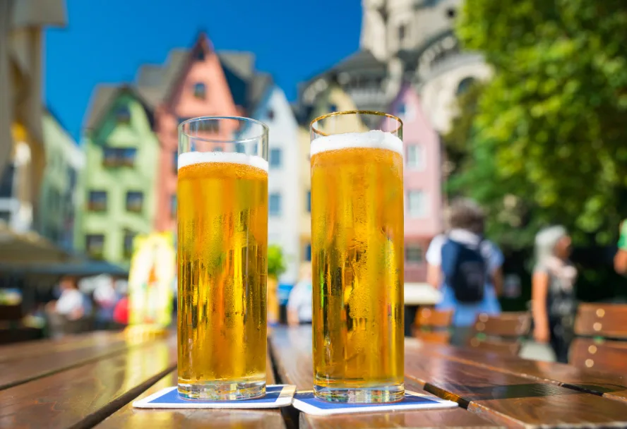 Zwei Kölschstangen auf einem Biergartentisch vor den bunten Häusern am Fischmarkt