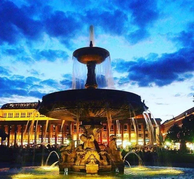 Der beleuchtete Brunnen auf dem Schlossplatz zur blauen Stunde, dahinter der Königsbau