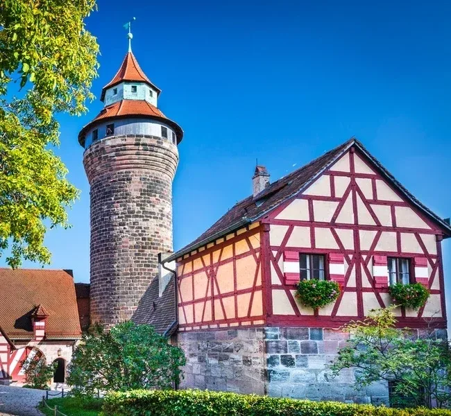 Der runde Sinwellturm der Kaiserburg neben einem rot-weißen Fachwerkhaus
