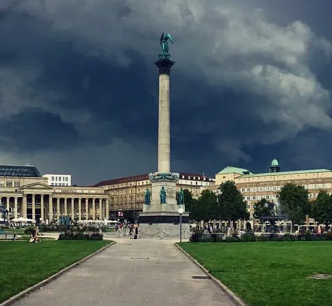 Der Schlossplatz mit der Jubiläumssäule vor dunklen Wolken, dahinter der Königsbau